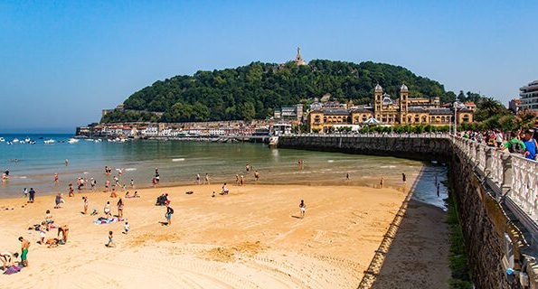 Playa con arena, gente disfrutando y un monte verde al fondo, con edificios cerca del mar de SAN SEBASTIAN