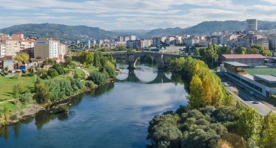 Vista panorámica de un río que fluye junto a una ciudad con montañas al fondo.