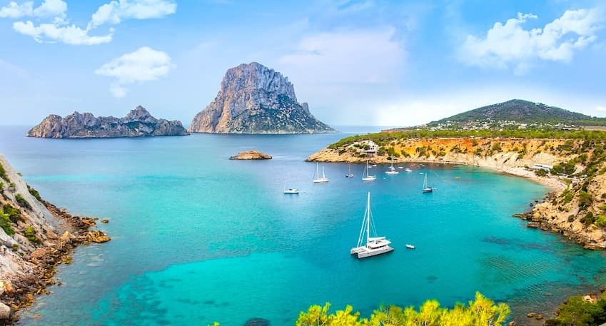 Vista panorámica de una cala en Ibiza con aguas turquesas y un islote en el fondo en ibiza