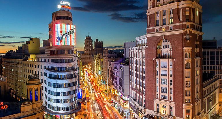 Vista nocturna de una animada calle urbana iluminada por neones y edificios emblemáticos.