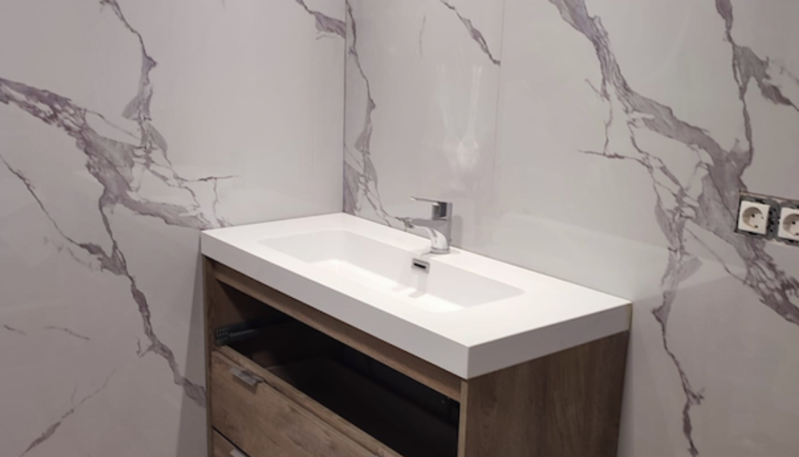 Baño moderno con lavabo de mármol blanco brillante y una ventana grande.