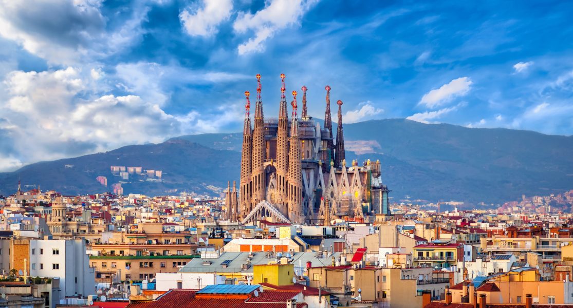 Sagrada Familia en Barcelona con cielo azul y nubes. Montañas al fondo.