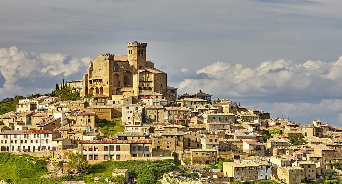 Castillo en lo alto de una colina rodeado de casas y nubes en el cielo de PAMPLONA