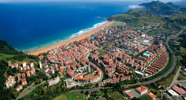 Vista aérea de un pueblo costero con playa y montañas alrededor en Gipúzkoa