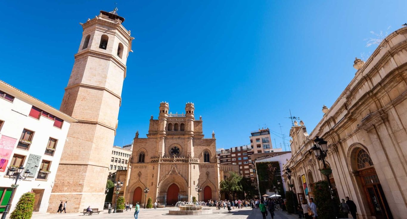 Plaza con una iglesia gótica y una torre campanario, bajo un cielo azul claro en Castellón de la Plana.