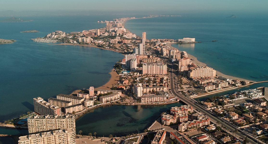 Vista aérea de una ciudad costera, con edificios y carretera junto al mar.