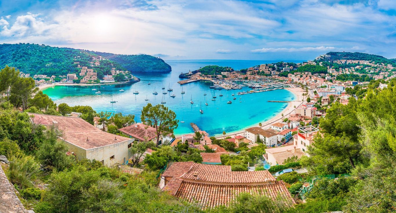 Vista panorámica de una bahía con aguas turquesas y barcos, rodeada de casas y vegetación.