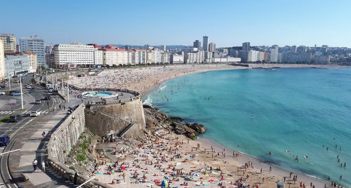 Playa con muchas personas, edificios al fondo y mar azul. Día soleado en A CORUÑA